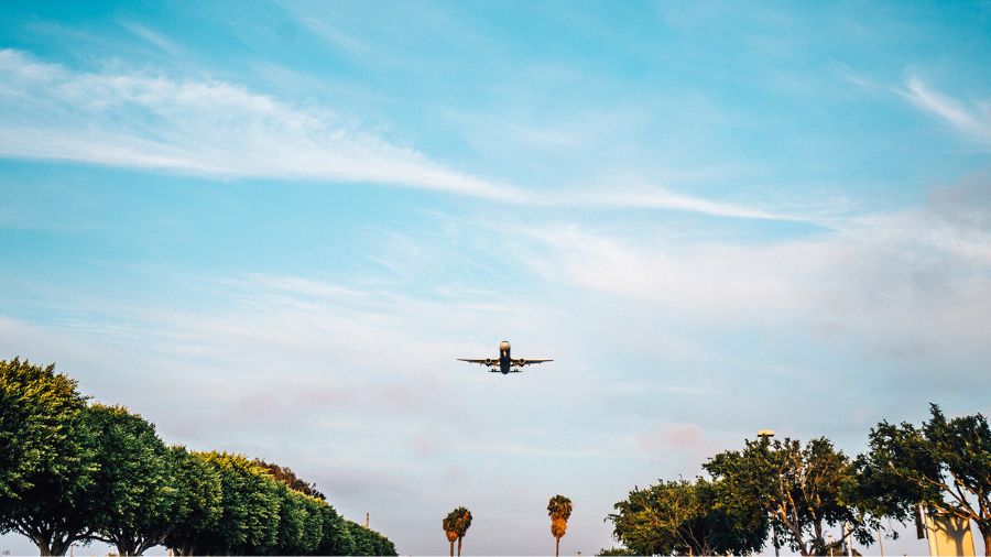 Aeroplane against cloudy blue sky descends for landing onto tree-lined runway