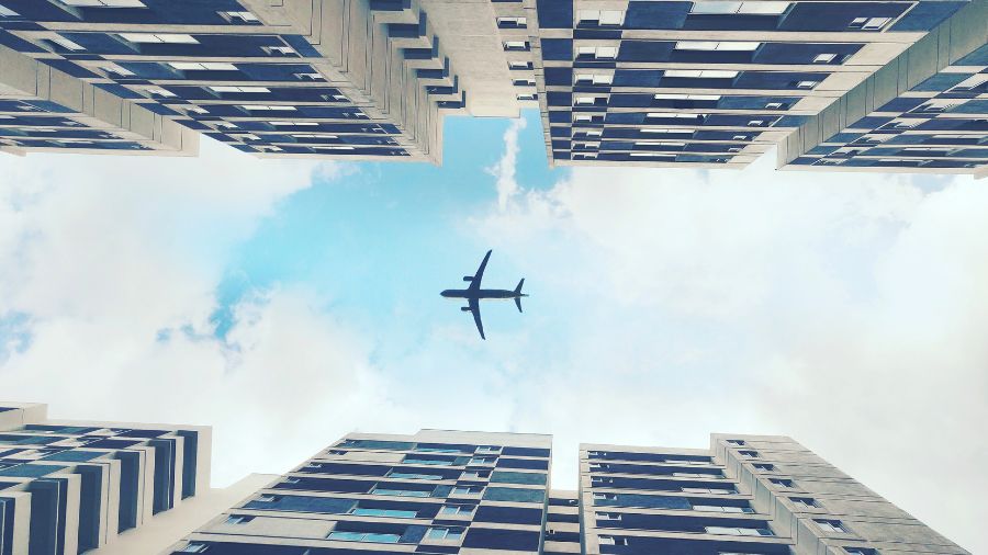 Aeroplane against cloudy blue sky descends for landing onto tree-lined runway