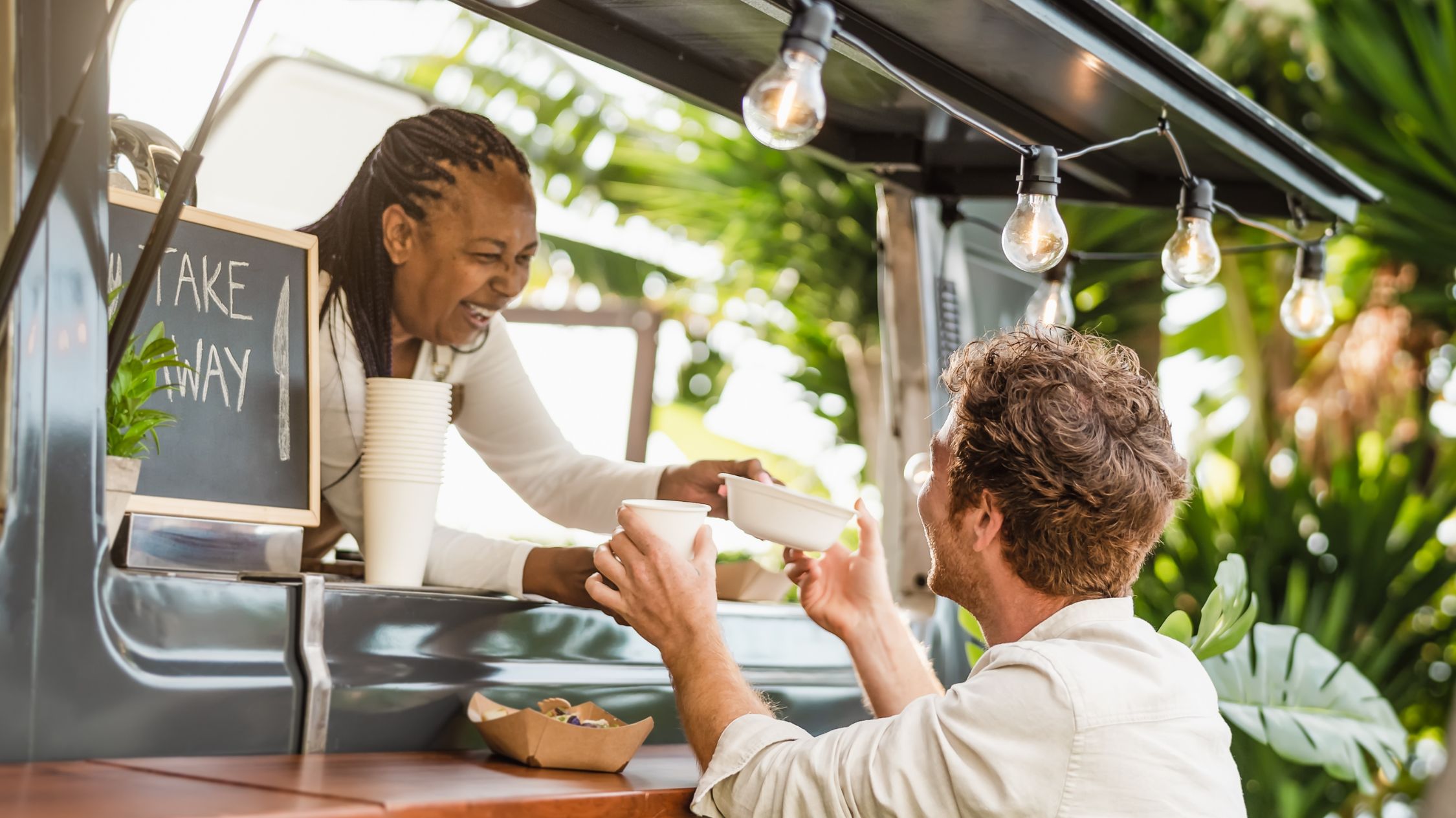 a tourist takes a dish from a smiling street food vendor